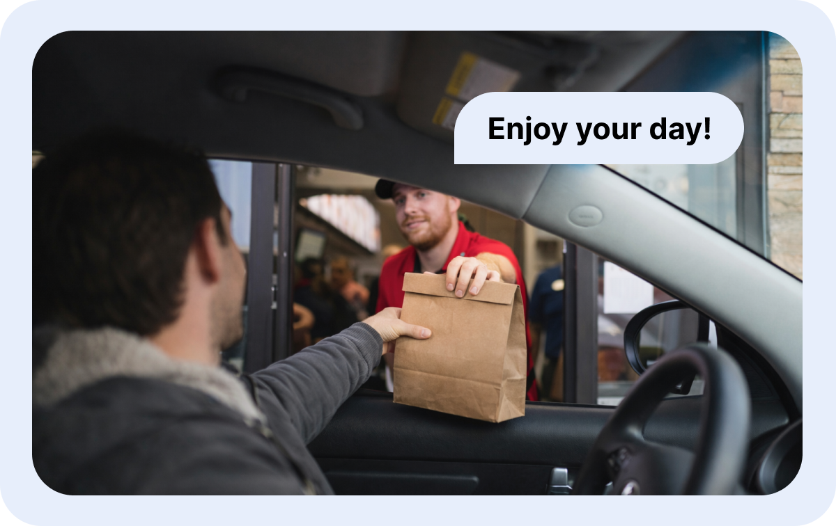 A drive-thru employee hands a completed order to a customer at the pickup window, illustrating the fast, friendly service enabled by AI order-taking technology.